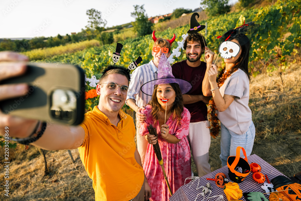 Obraz premium Joyful friends posing for a group selfie during an autumn Halloween gathering outdoors.