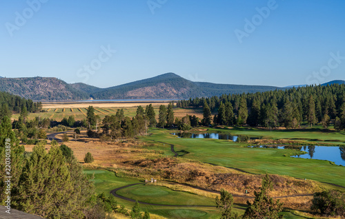 Manicured fairways of a golf course meet natural grasslands and a distant lake framed by forested mountains in Klamath Falls Oregon.