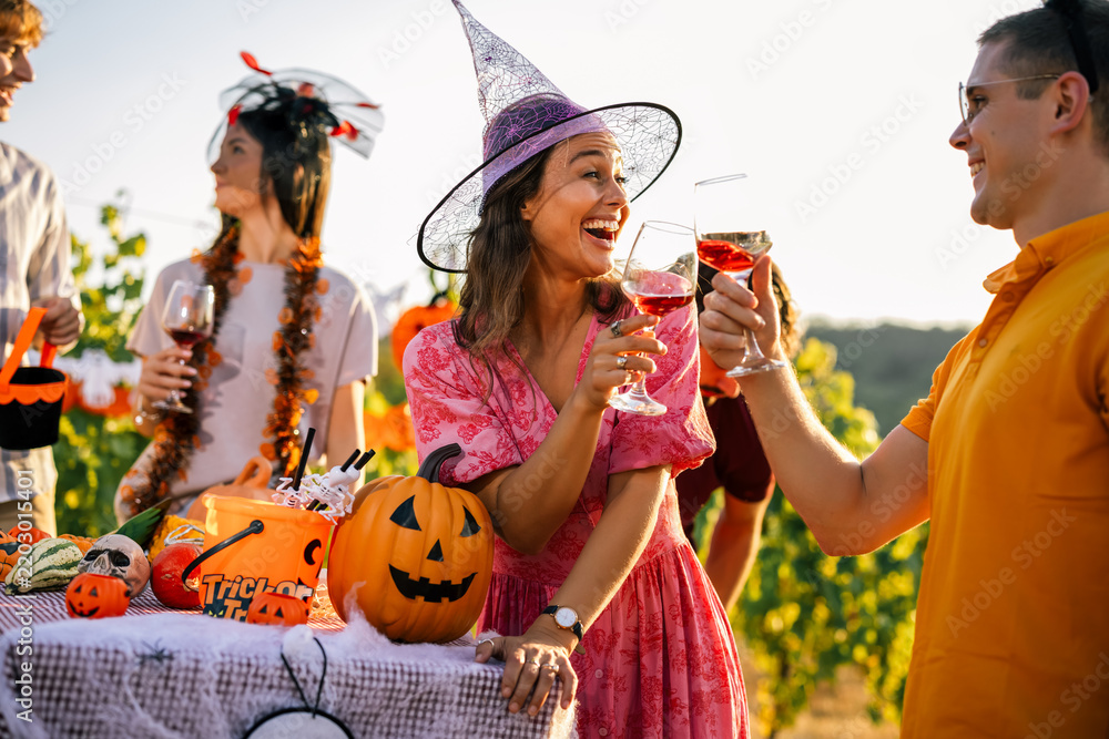 Obraz premium Woman in a witch hat clinking wine glasses with a friend at an outdoor Halloween party.