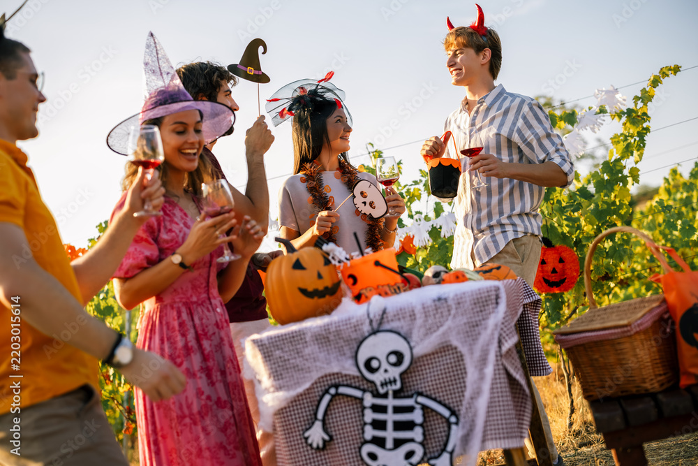 Obraz premium Cheerful young people enjoying drinks and conversation at an outdoor Halloween party.