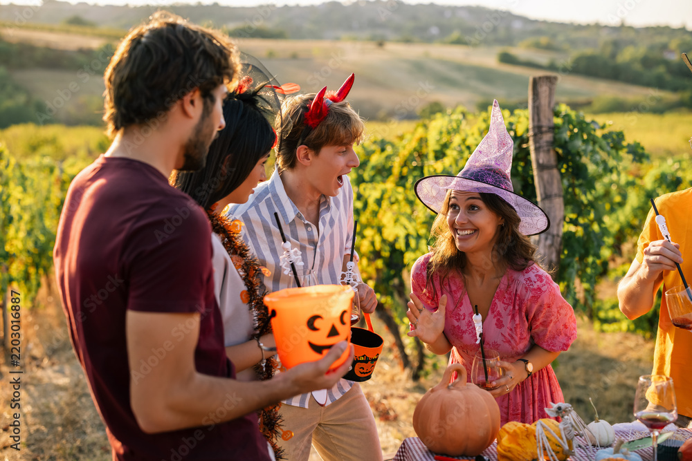 Obraz premium Excited young woman in a witch hat talking to her friends at a Halloween vineyard party.
