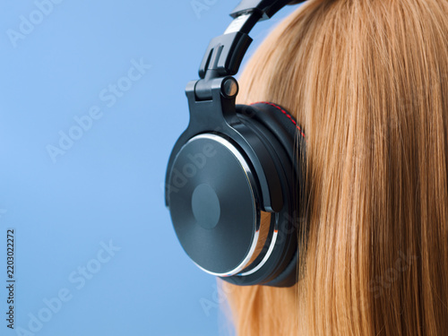 Close-up Side View of Redhead Girl Wearing Professional Black Headphones on Blue Background