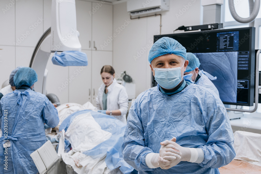 Fototapeta premium Cardiologist looking at the camera with a patient and medical team working in the background.