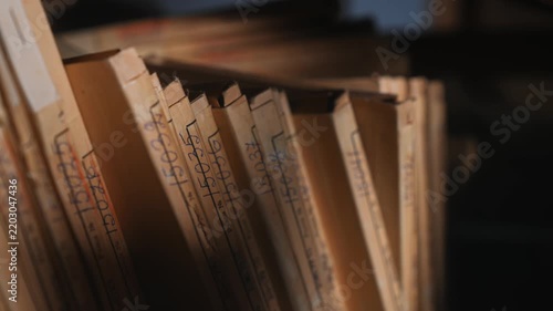 Old archive folders with radio reel recordings stand on wooden shelves in warm light. Concept of audio preservation, media history, library, research, heritage, broadcast archive.