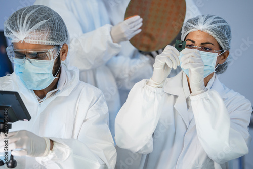 Obraz na płótnie A team of researchers in protective suits inspects electronic components and silicon wafers in a cleanroom