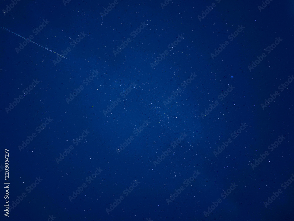 Fototapeta premium Cielo nocturno de color azul oscuro profundo salpicado de diminutas estrellas brillantes, transmitiendo serenidad, inmensidad y misterio cósmico.