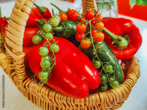 Фотография Fresh red peppers, cucumbers, tomatoes, and green fruits arranged in a woven bas