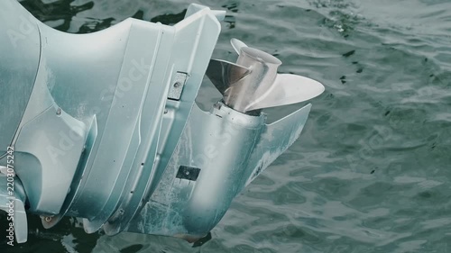 close-up view of stainless propeller and gearcase housing lifted above calm rippling water under daylight soft