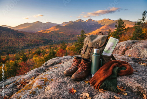 Hiking boots, backpack, and thermos resting on rocky mountain cliff.