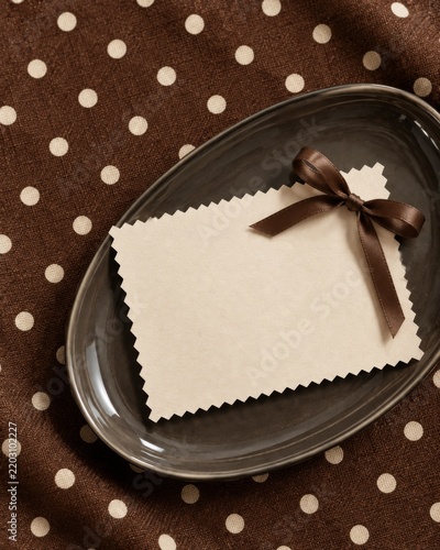 A Blank Card on a Plate Resting on a Brown Polka Dot Tablecloth
