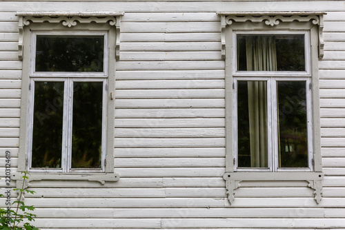Old white windows with carved casings in wooden siding wall