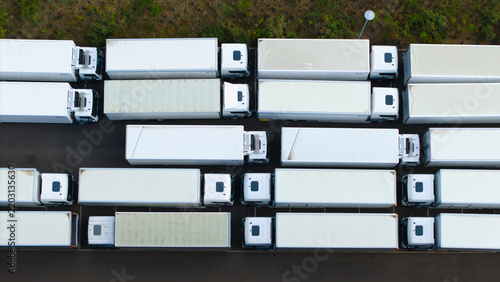 Aerial view of a logistics hub with rows of white semi-trailer trucks parked in an industrial yard in Bedford, England, United Kingdom.