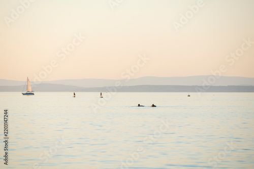 A peaceful summer day at Lake Balaton: sailboat, paddleboards, and swimmers