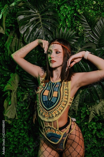 Go-go dancer posing in colorful stage costume with face gems against lush green tropical decor in a nightclub, creating a vibrant image for nightlife, dance and event promotion