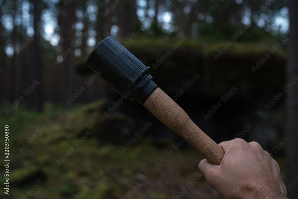 Obraz premium ​A close-up photograph of a hand holding a wooden and 3D printed replica of a WWII German Stielhandgranate stick grenade in a deep forest.