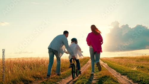 Foto Dad mom helping child ride bicycle