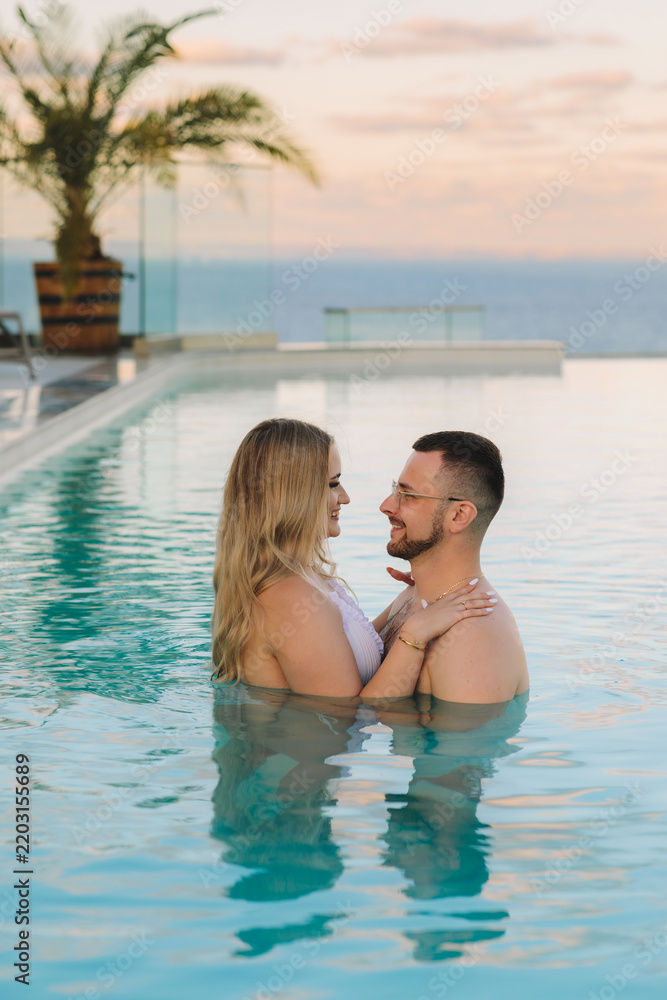 Fototapeta premium Romantic couple embracing in an infinity pool at sunset, luxury tropical resort with panoramic ocean view, honeymoon travel and vacation concept, high quality photo