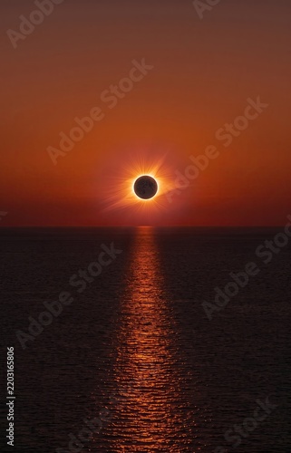 Stunning total solar eclipse glowing over calm ocean reflecting fiery red light