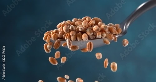 Wheat grains falling from spoon in slow motion on blue background