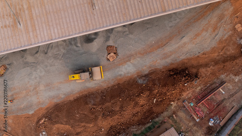 Aerial view of Kawasan Industri Terpadu Batang with a yellow road roller compacting gravel and soil at a construction site in Kecamatan Gringsing, Jawa Tengah, Indonesia.