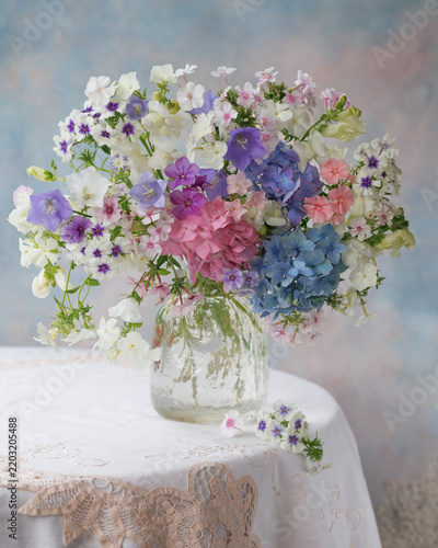 Beautiful bouquet of phlox, hydrangeas, and bellflowers in a vase on a table; close-up still life, blur, selective focus.