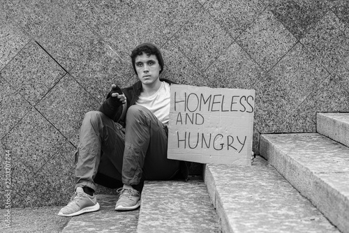Obraz na plátně Homelessness and poverty crisis, young man begging for help with a sign on city