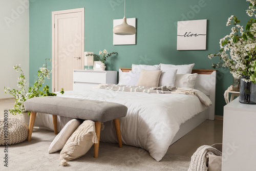Comfortable bed, bench and vases with blooming tree branches in bedroom