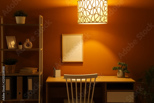 Interior of dark office with workplace, shelf unit and glowing lamp