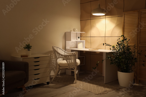 Interior of stylish office with workplace and glowing lamp in evening