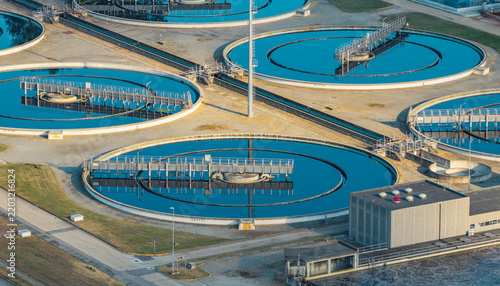 Aerial view of multiple circular clarifiers with rotating bridge systems at a large wastewater treatment facility in Italy.