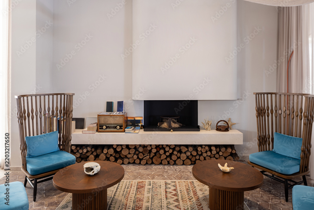 Obraz premium Cozy hotel fireplace lounge with wooden chairs coffee tables and stacked firewood