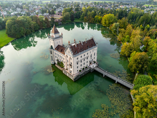 Aerial view of Schloss Anif, a historic water castle surrounded by a lush green lake, dense trees, and a wooden bridge in Anif, Salzburg, Austria.