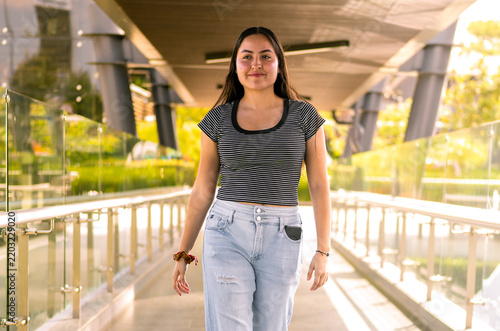 Fotografie Young woman walking confidentially on modern city bridge
