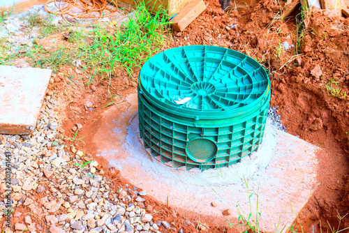 Green septic tank drainage utility structure is placed in ground at construction site among soil gravel.