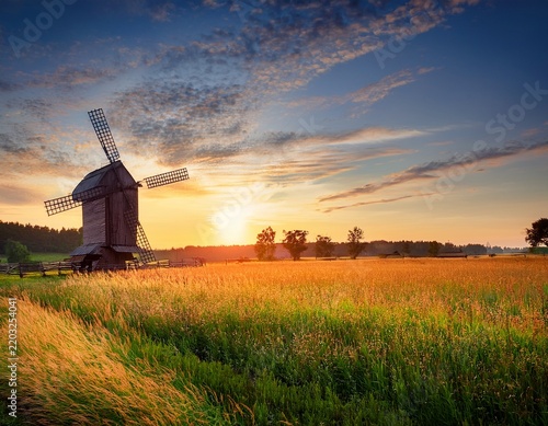 old windmill at sunrise in a rural field with a wooden farm landscape and meadow grass this peaceful agriculture scene shows
