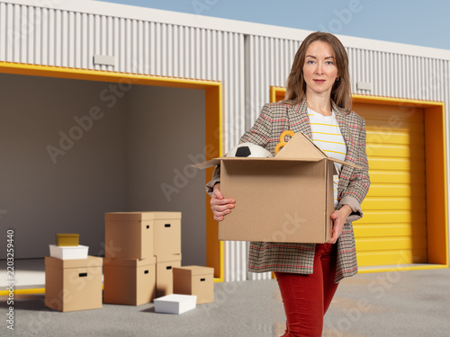 Картината върху платно Self storage service, woman carries a box of personal belongings into a rented storage unit during moving, relocation and temporary property storage