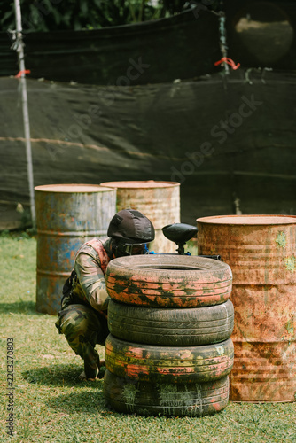 Paintball Player Crouching Behind Tire Barricade in Action