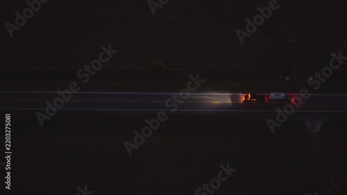 High angle view of vehicles driving on country road at twilight, illuminated by headlamps, capturing motion, travel and peaceful rural scenery.