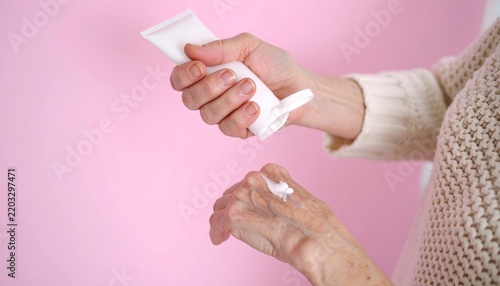 Elderly Woman Applying Moisturizing Hand Cream Against Pink Background