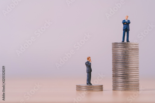 Income inequality concept with miniature businessmen standing on different stacks of coins symbolizing wealth gap, salary disparity, financial inequality, career success and economic opportunity.