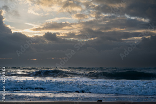 Dramatic sunset sky with sunbeams over ocean waves breaking on the shore