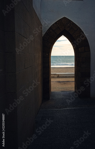 Stone archway framing a view of the beach and sea at dusk