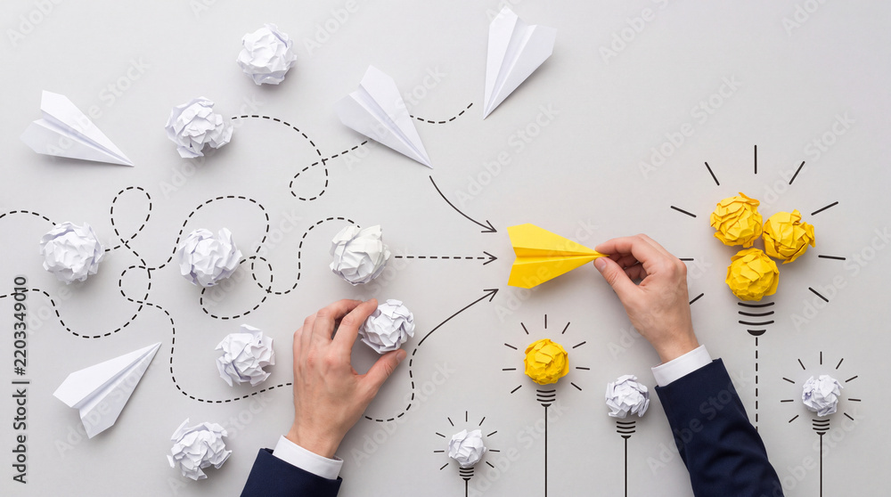 Fototapeta premium Creative business strategy and innovation concept with hands holding a yellow paper plane and crumpled papers transformed into light bulbs representing successful solution and new ideas.