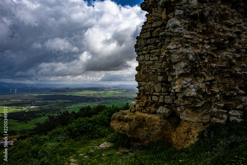 Ancient castle stone wall overlooking a green valley under cloudy skies, Spain