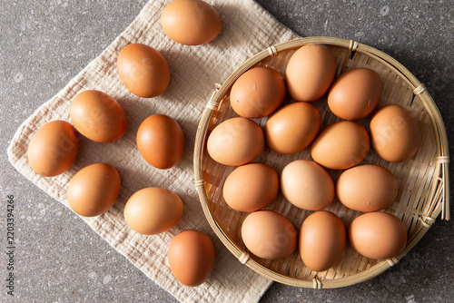Fresh raw brown eggs displayed in a round bamboo basket on rustic linen cloth, top view