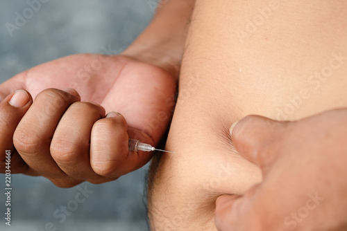 Close up of a person self administering a subcutaneous injection with a small syringe into their abdomen, representing diabetes management, concept medical treatment, and healthcare.