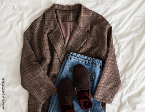 A checkered blazer, blue jeans, brown suede loafers on a light background, top view. Comfortable women's casual clothing