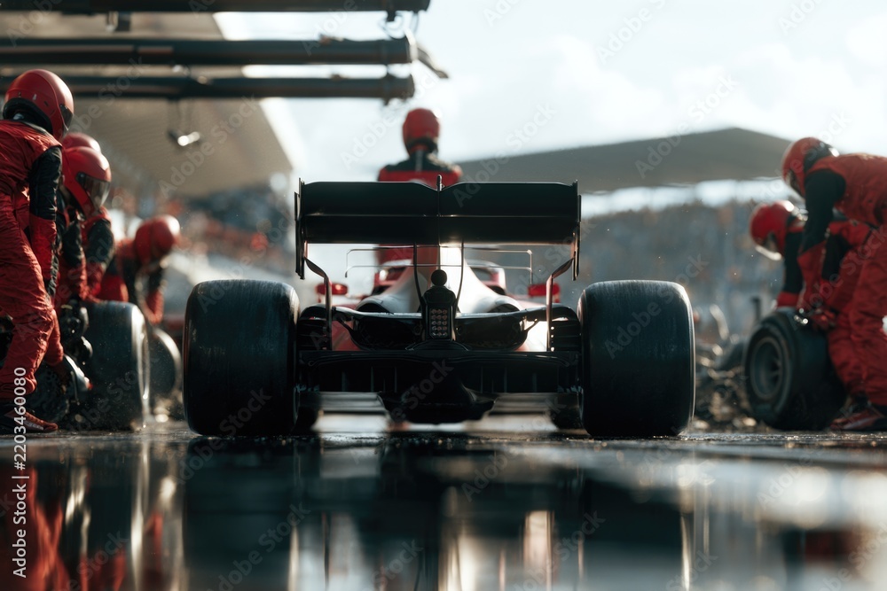 Obraz premium A Formula 1 race car is serviced by a pit crew in red uniforms during a pit stop on a wet track.