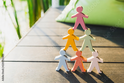 Leadership and teamwork hierarchy concept, colorful human figures stacked in pyramid on wooden deck in sunlight, representing corporate organization, career growth, and talent structure.