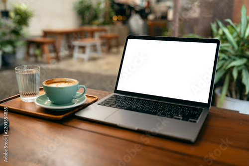 Laptop computer with blank white screen mockup on wooden table in a coffee shop with a cup of latte.